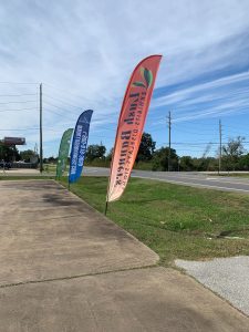 10ft double-sided feather flag outside a coffee shop with ‘Now Open’ and a special offer, mounted on a metal square base.